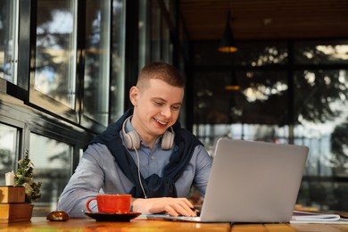 Young male student with laptop studying at table in cafe