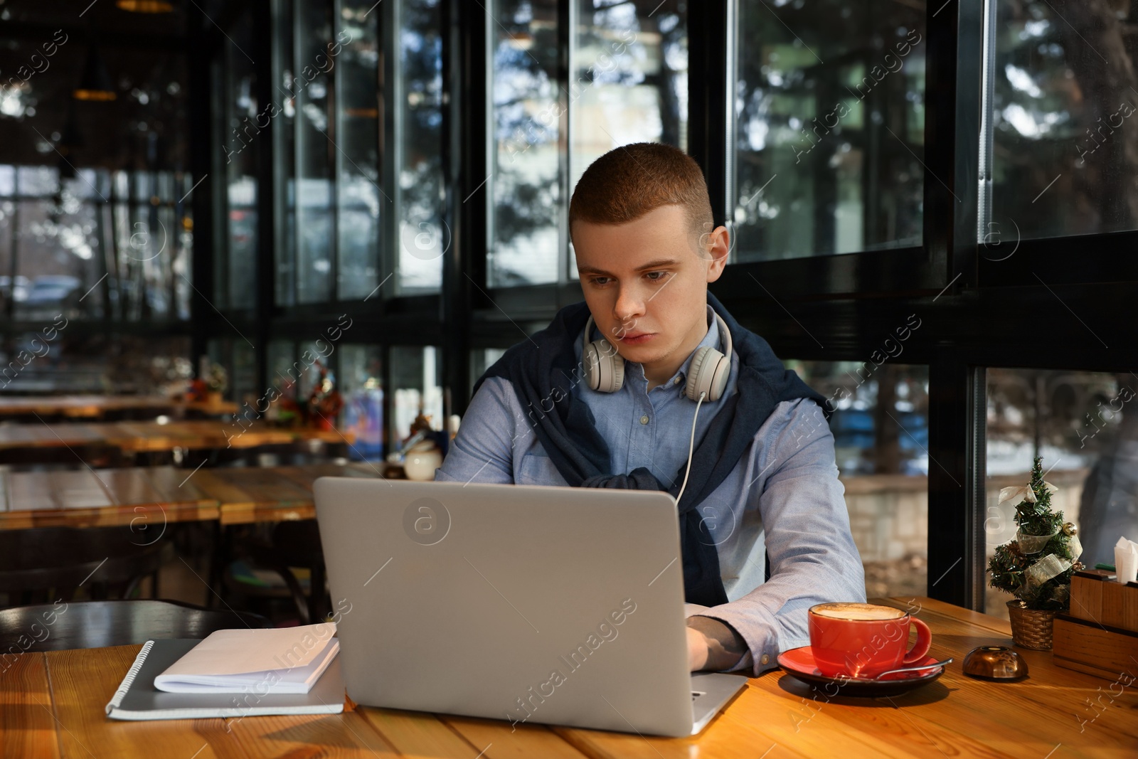 Photo of Young male student with laptop studying at table in cafe