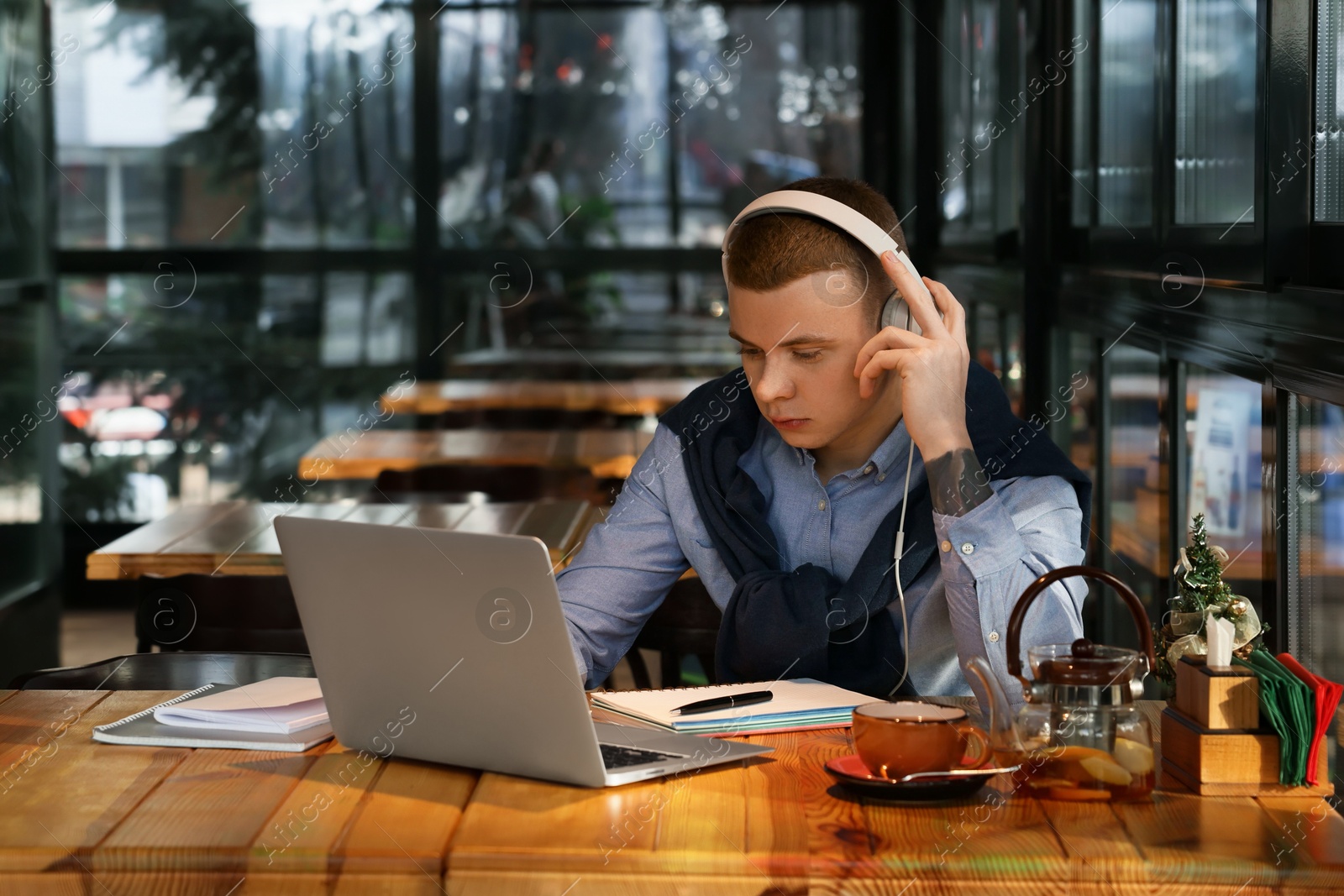 Photo of Young male student with laptop and headphones studying at table in cafe