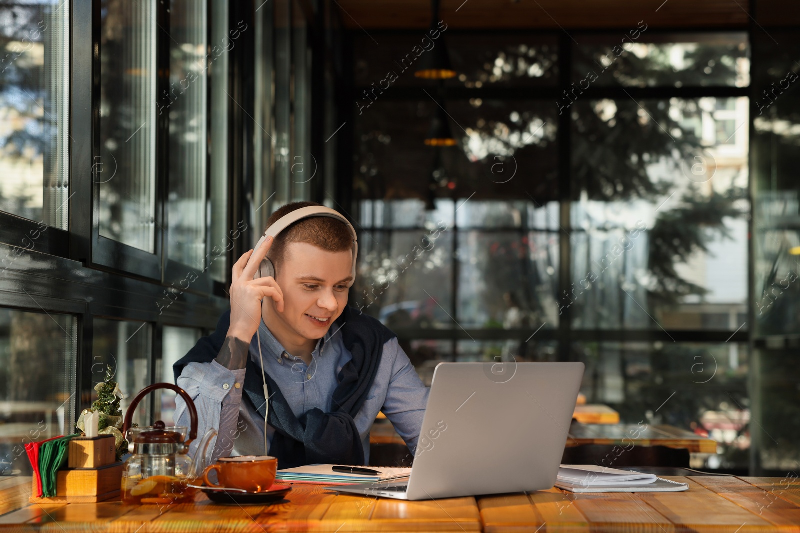 Photo of Young male student with laptop and headphones studying at table in cafe