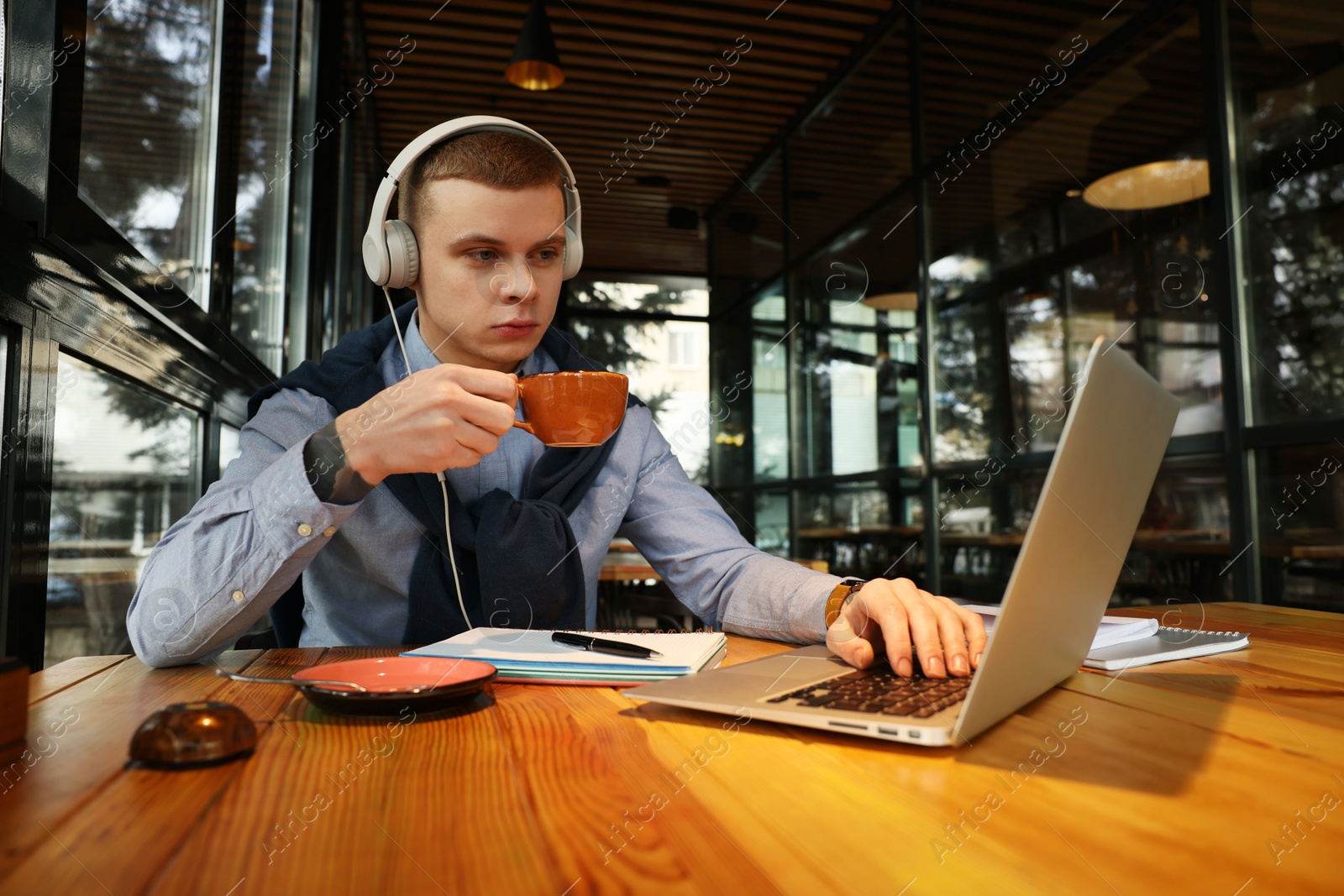 Photo of Young male student with laptop drinking coffee while studying at table in cafe