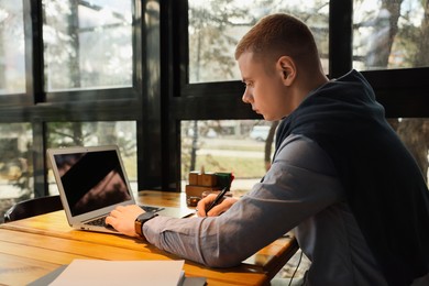 Photo of Young male student with laptop studying at table in cafe