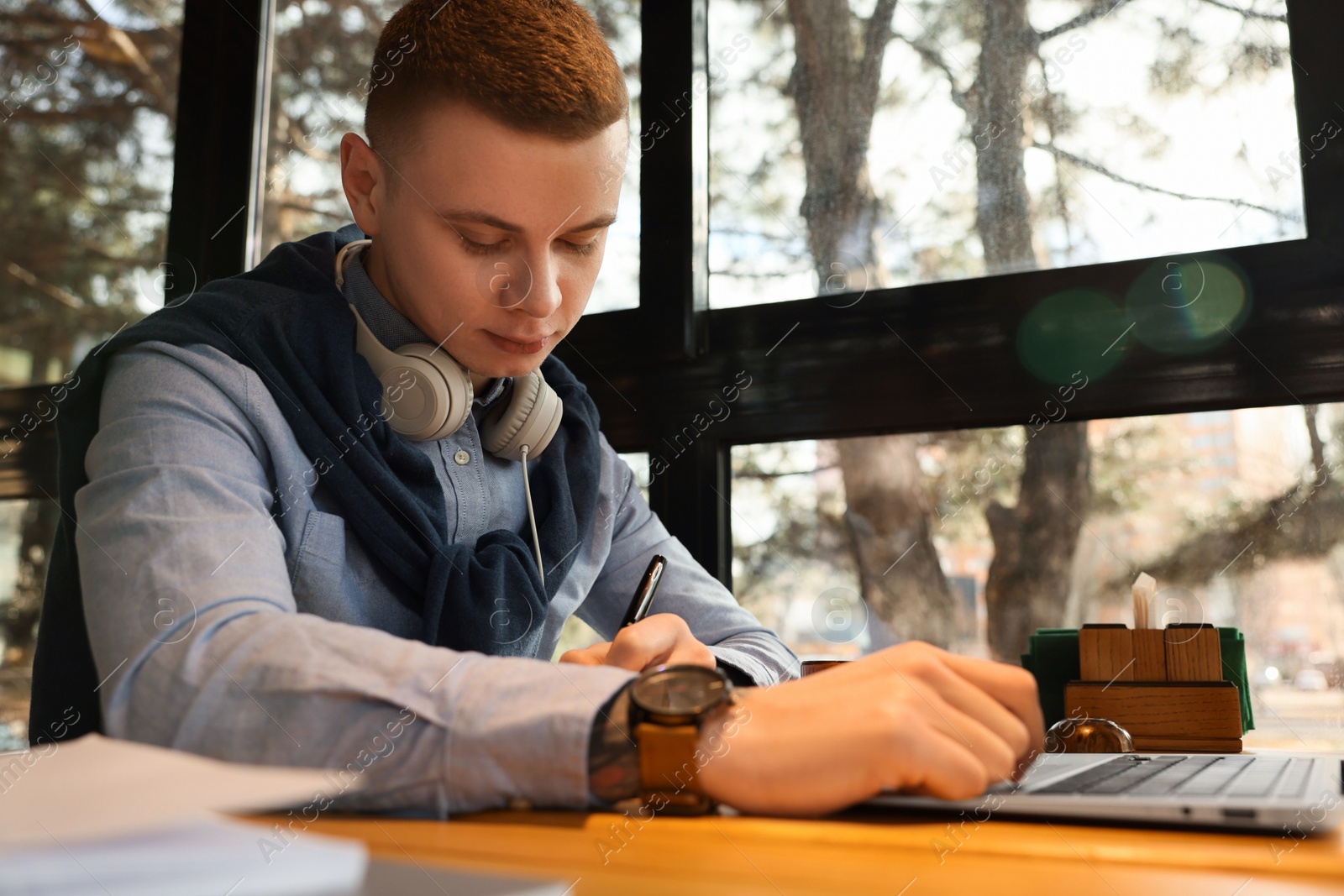 Photo of Young male student with laptop studying at table in cafe