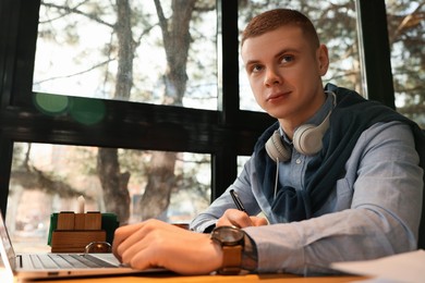 Young male student with laptop studying at table in cafe