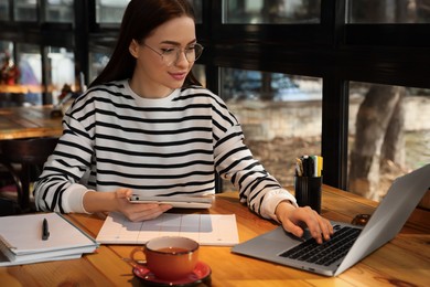 Photo of Young female student with laptop and tablet studying at table in cafe