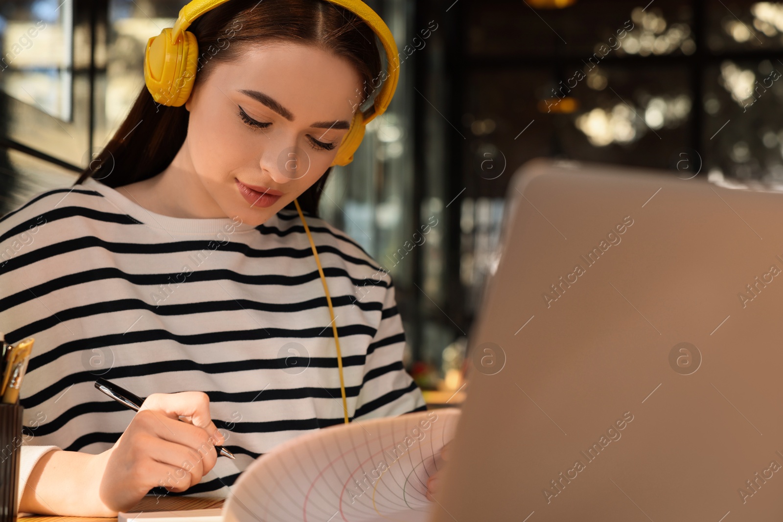 Photo of Young female student with laptop and headphones studying at table in cafe