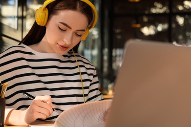 Photo of Young female student with laptop and headphones studying at table in cafe