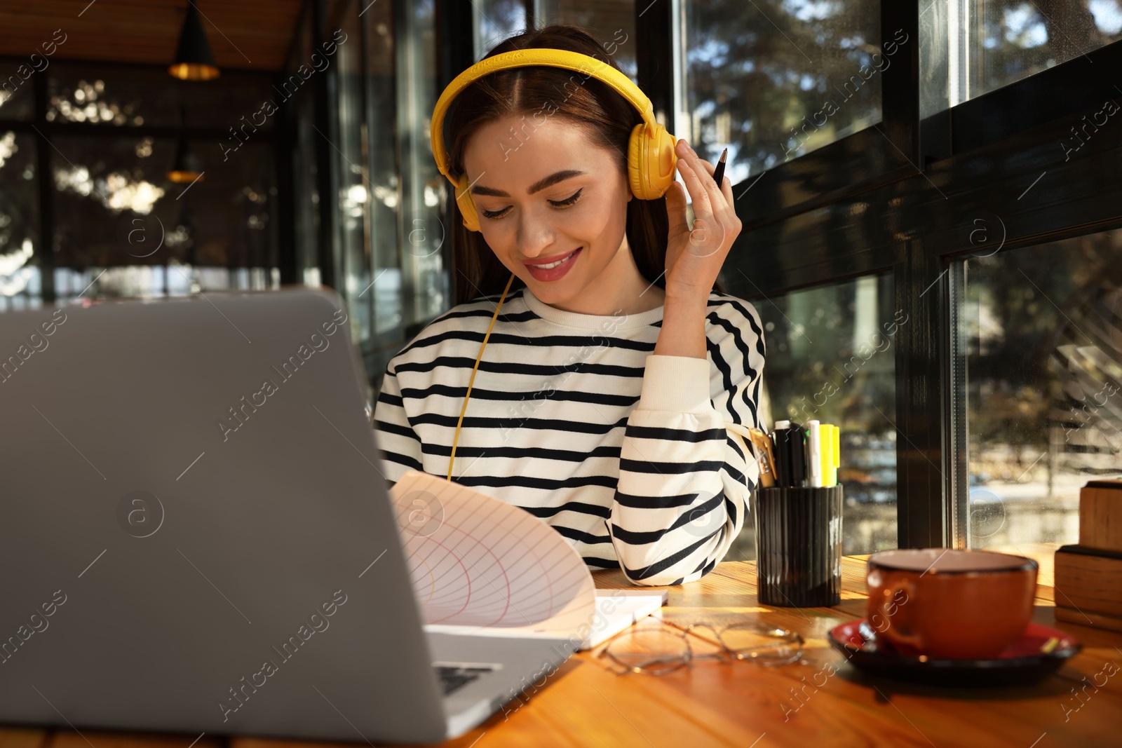 Photo of Young female student with laptop and headphones studying at table in cafe