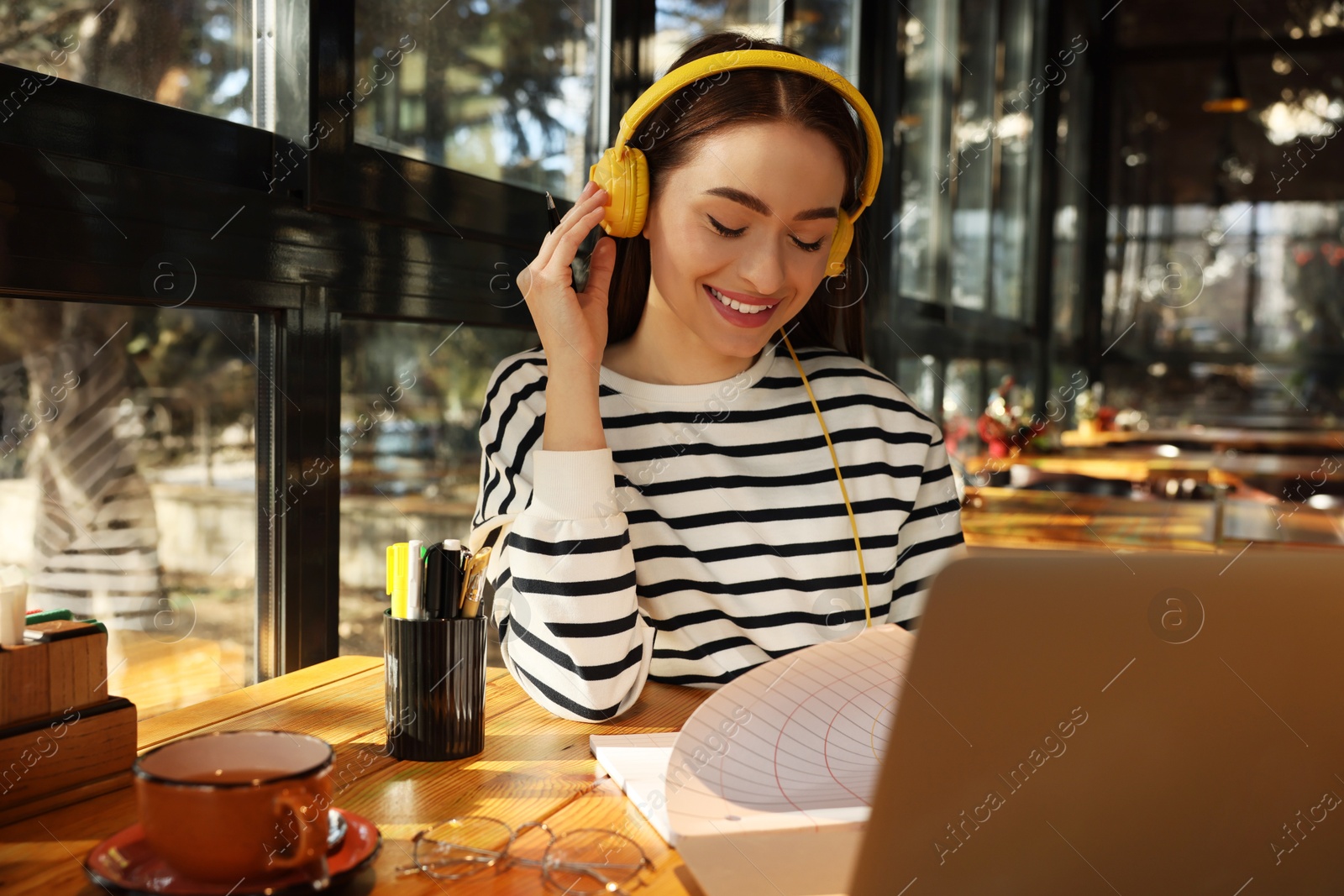 Photo of Young female student with laptop and headphones studying at table in cafe