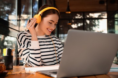 Photo of Young female student with laptop and headphones studying at table in cafe