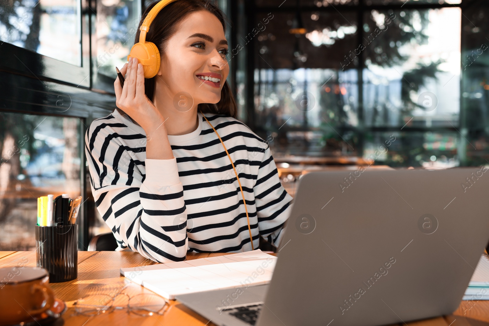 Photo of Young female student with laptop and headphones studying at table in cafe