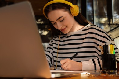 Photo of Young female student with laptop and headphones studying at table in cafe