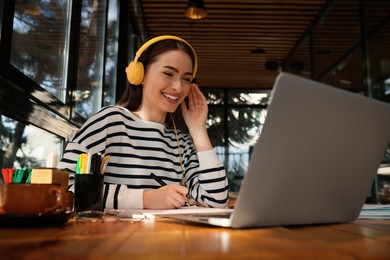 Photo of Young female student with laptop and headphones studying at table in cafe