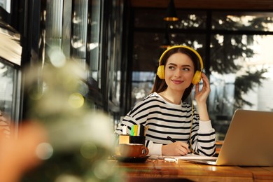 Photo of Young female student with laptop and headphones studying at table in cafe