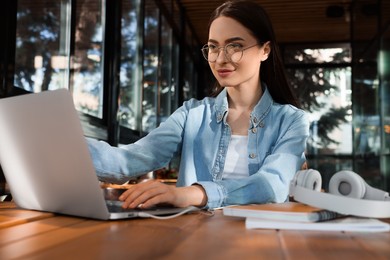 Young female student with laptop studying at table in cafe