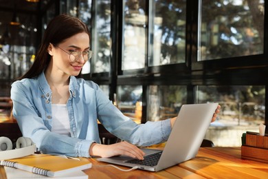 Young female student with laptop studying at table in cafe