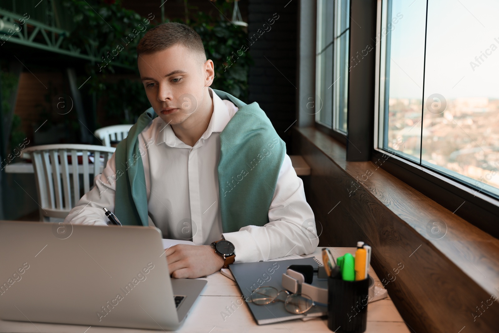 Photo of Young male student with laptop studying at table in cafe