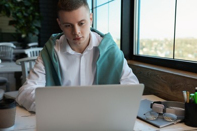 Young male student with laptop studying at table in cafe