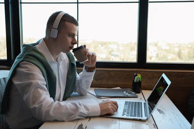 Young male student with laptop drinking coffee while studying at table in cafe