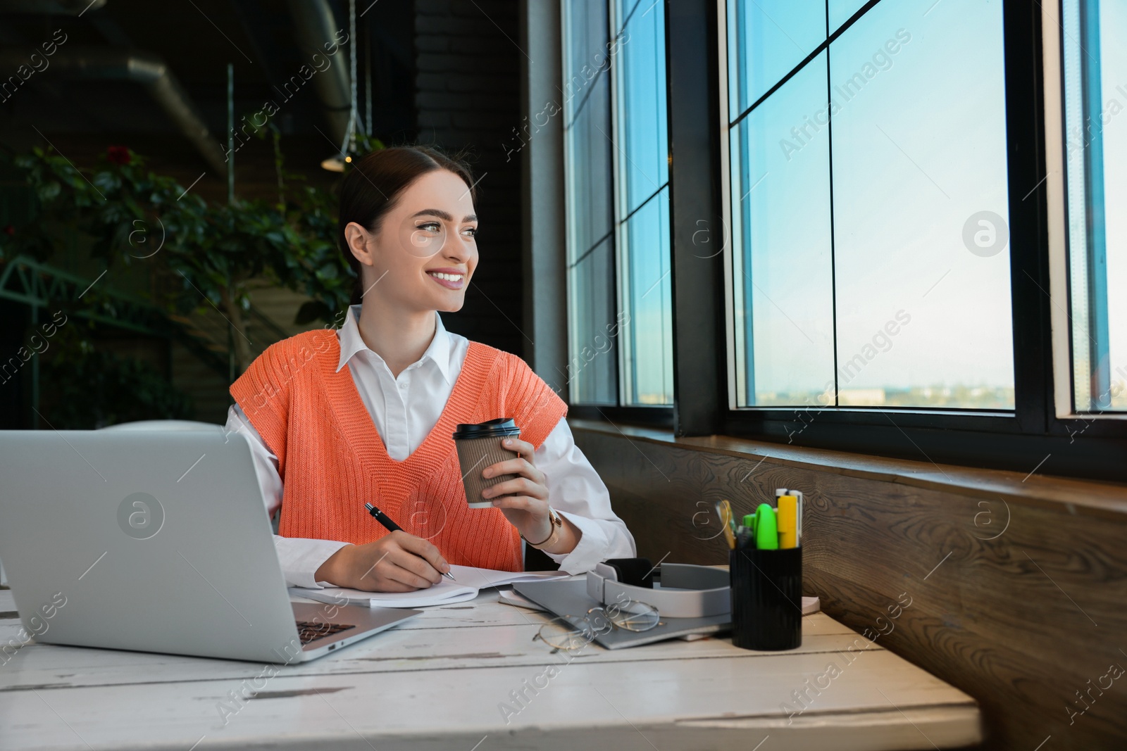 Photo of Young female student with laptop drinking coffee while studying at table in cafe