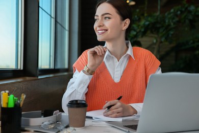 Young female student with laptop studying at table in cafe