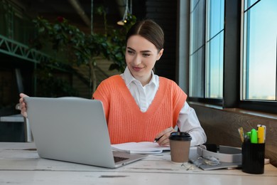 Young female student with laptop studying at table in cafe