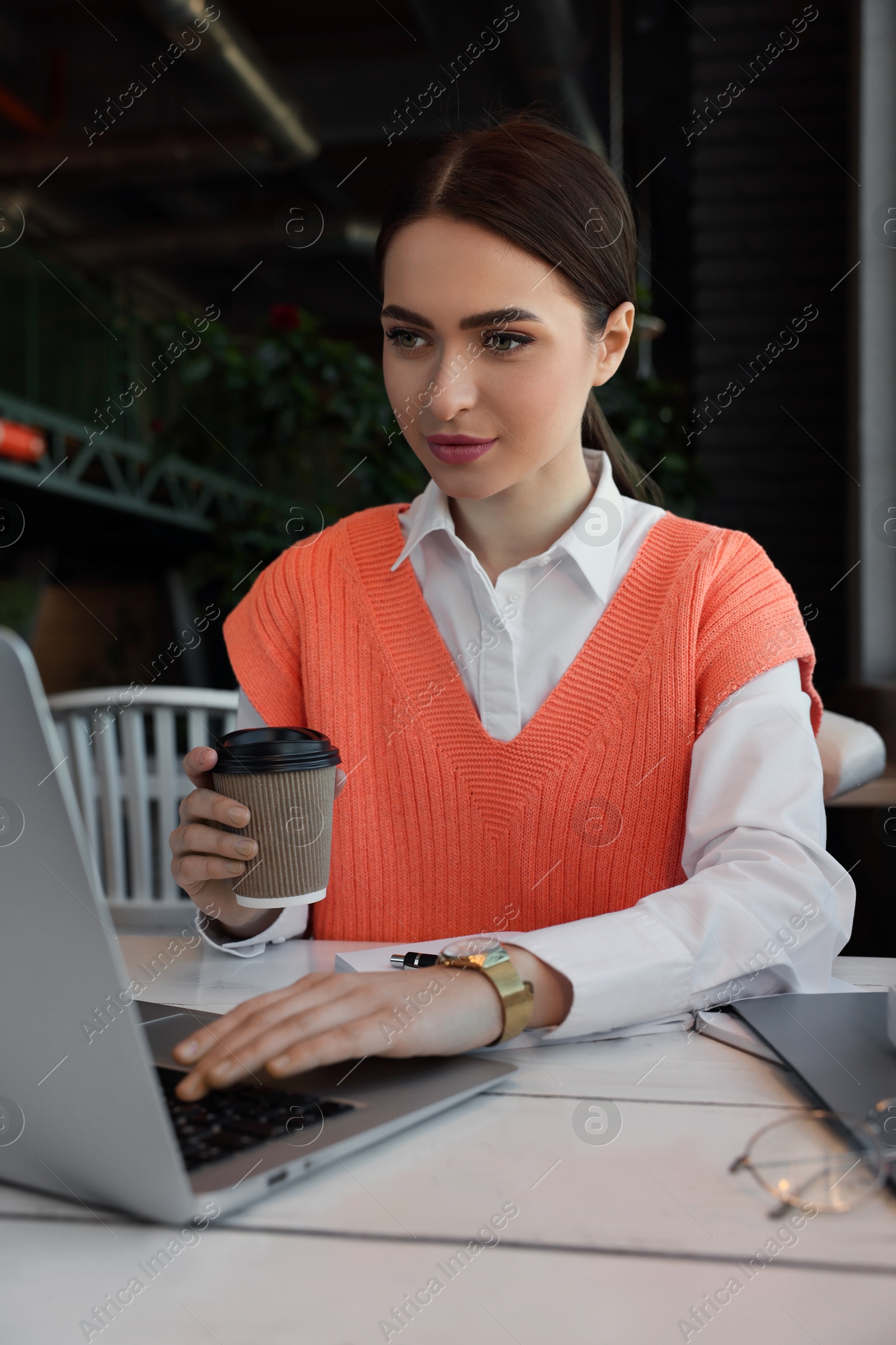 Photo of Young female student with laptop and coffee studying at table in cafe