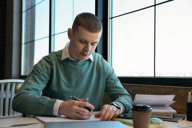 Photo of Young male student with notebooks studying at table in cafe