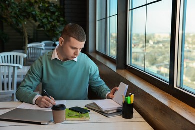 Young male student with notebooks studying at table in cafe