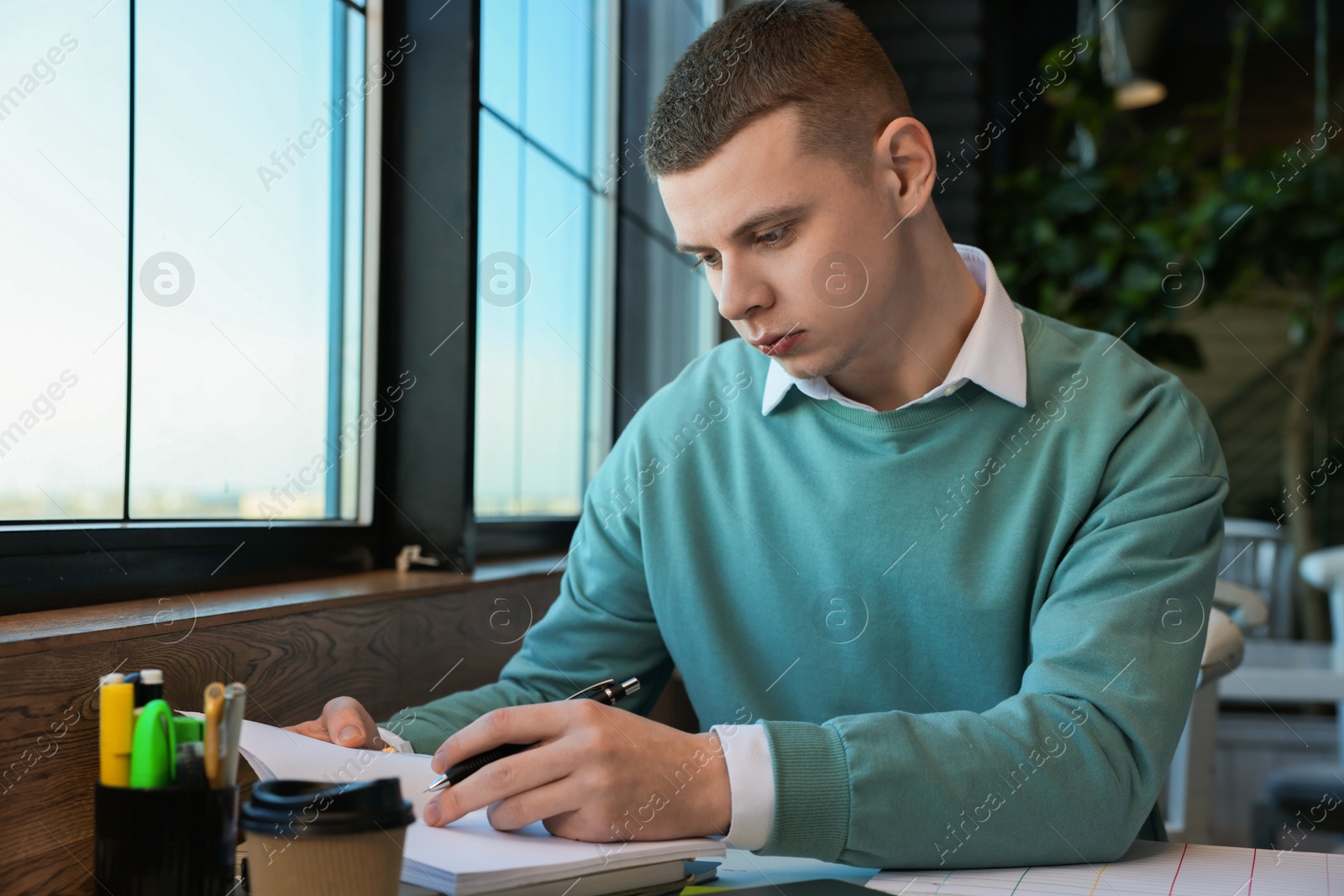 Photo of Young male student with books studying at table in cafe