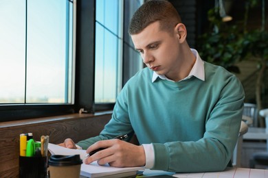 Young male student with books studying at table in cafe