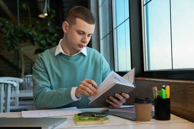 Young male student with notebooks studying at table in cafe