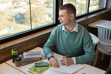 Photo of Young male student with books studying at table in cafe