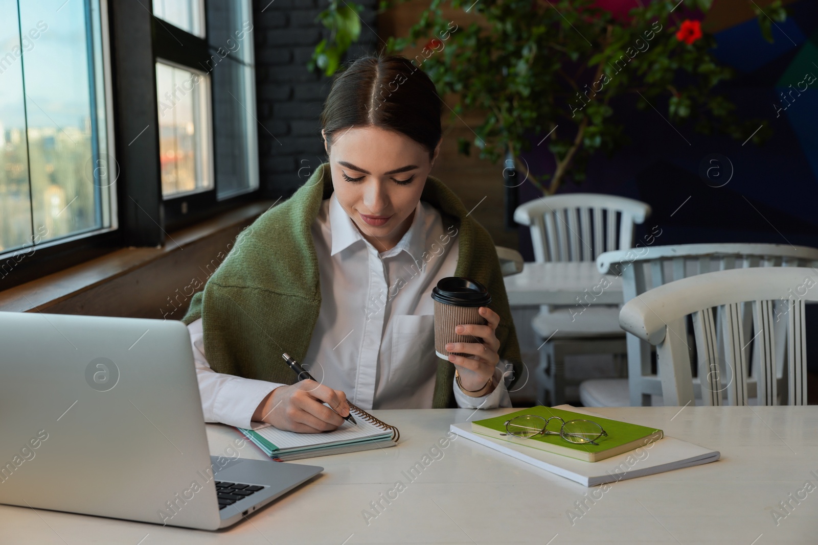 Photo of Young female student with laptop and coffee studying at table in cafe