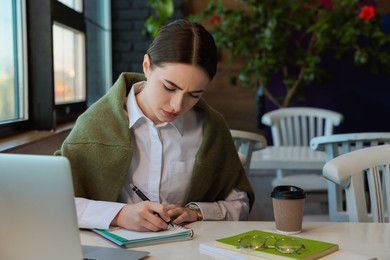 Young female student with laptop studying at table in cafe