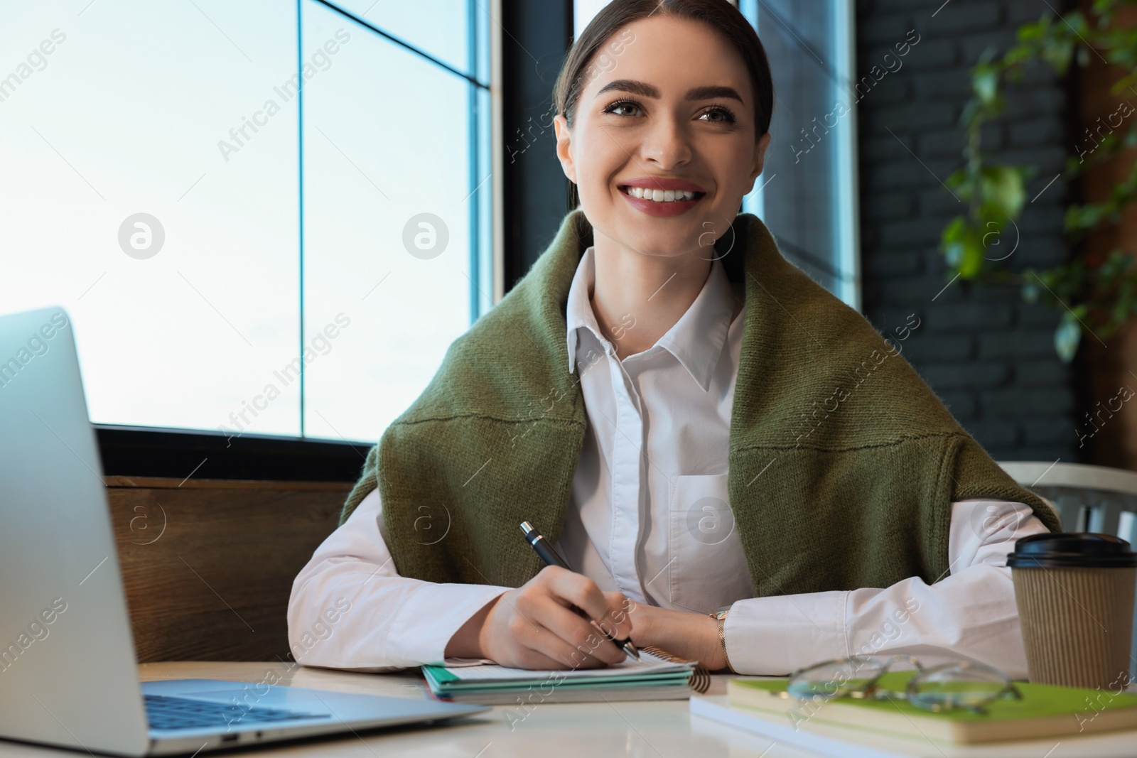 Photo of Young female student with laptop studying at table in cafe