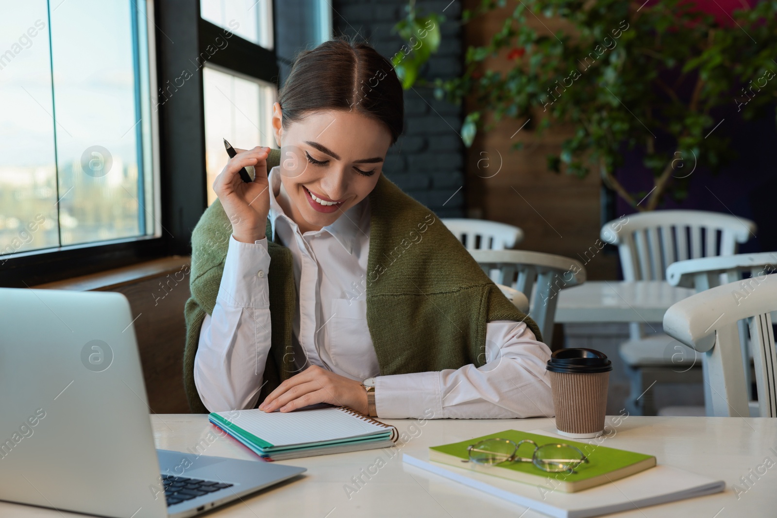 Photo of Young female student with laptop studying at table in cafe