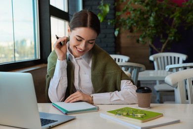 Young female student with laptop studying at table in cafe