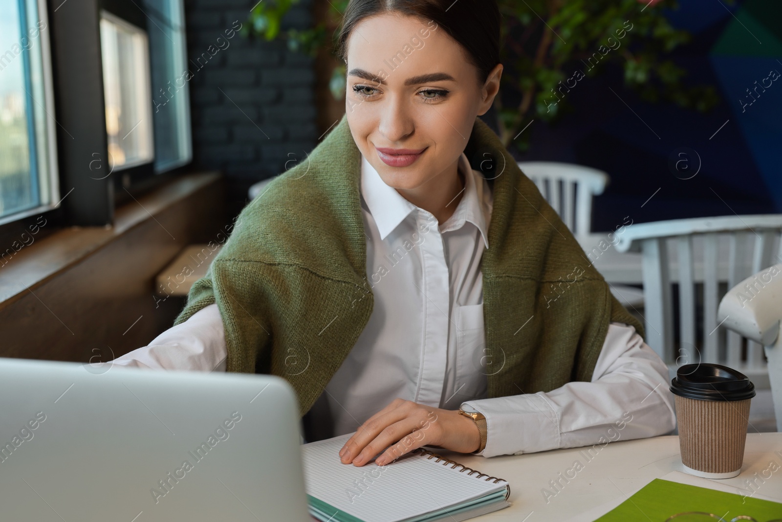 Photo of Young female student with laptop studying at table in cafe