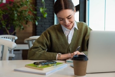 Young female student with laptop studying at table in cafe