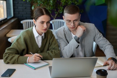 Photo of Young students with laptop studying at table in cafe