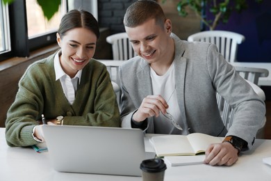 Photo of Young students with laptop studying at table in cafe