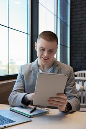 Young male student with tablet studying at table in cafe