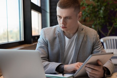 Photo of Young male student with laptop and tablet studying at table in cafe