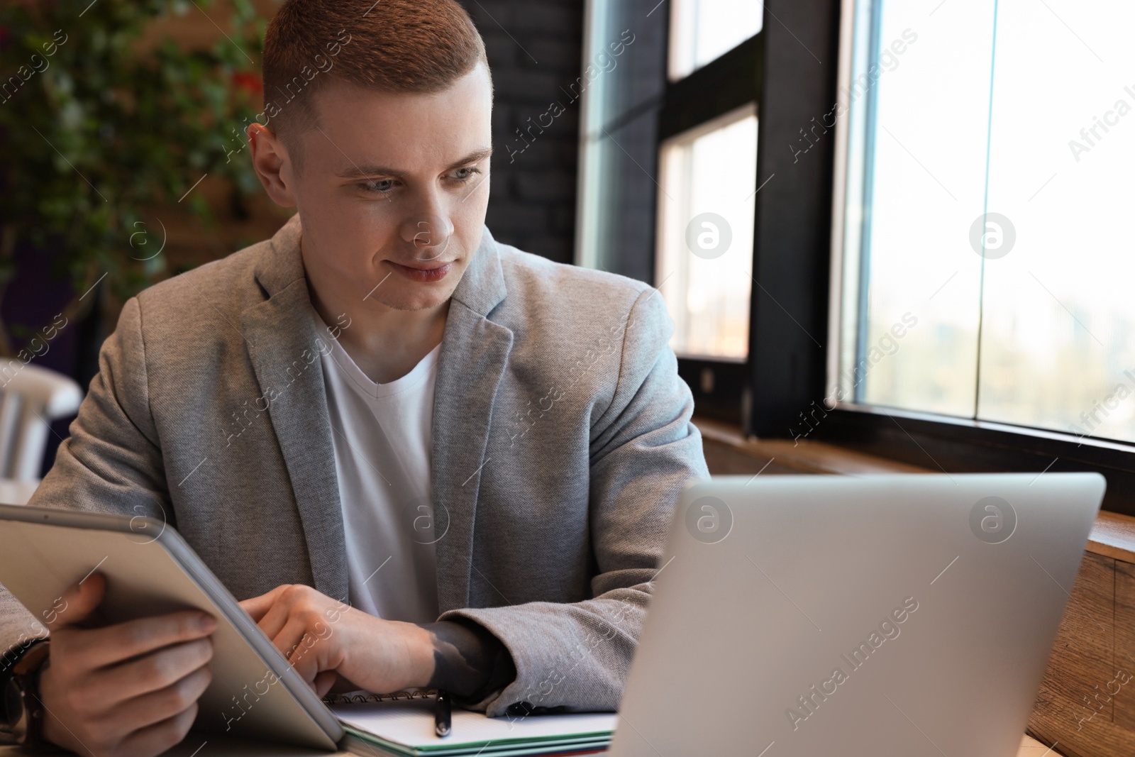 Photo of Young male student with laptop and tablet studying at table in cafe