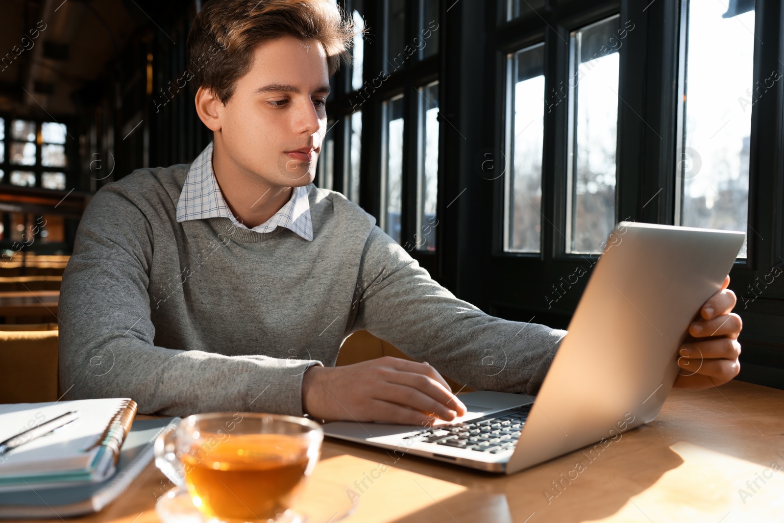 Photo of Teenage student with laptop studying at table in cafe