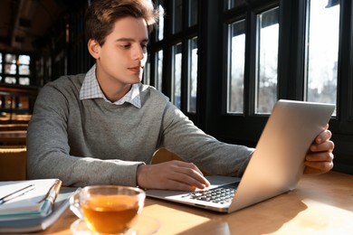 Photo of Teenage student with laptop studying at table in cafe