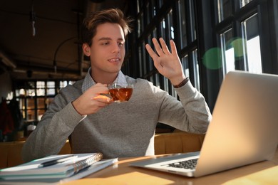 Teenage student with laptop using video chat while studying at table in cafe