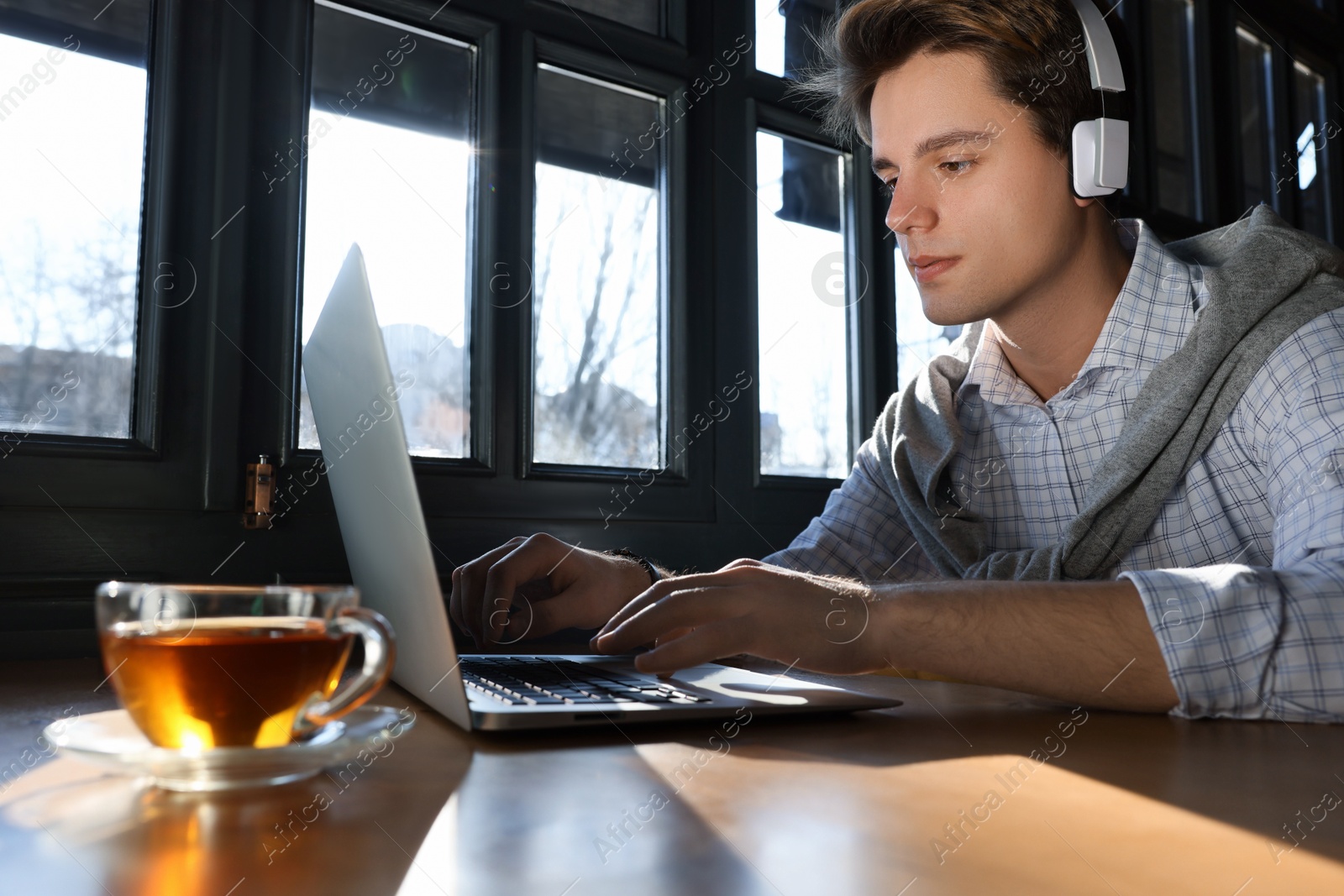 Photo of Teenage student with laptop and headphones studying at table in cafe