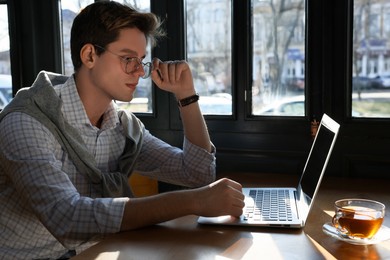 Teenage student with laptop studying at table in cafe